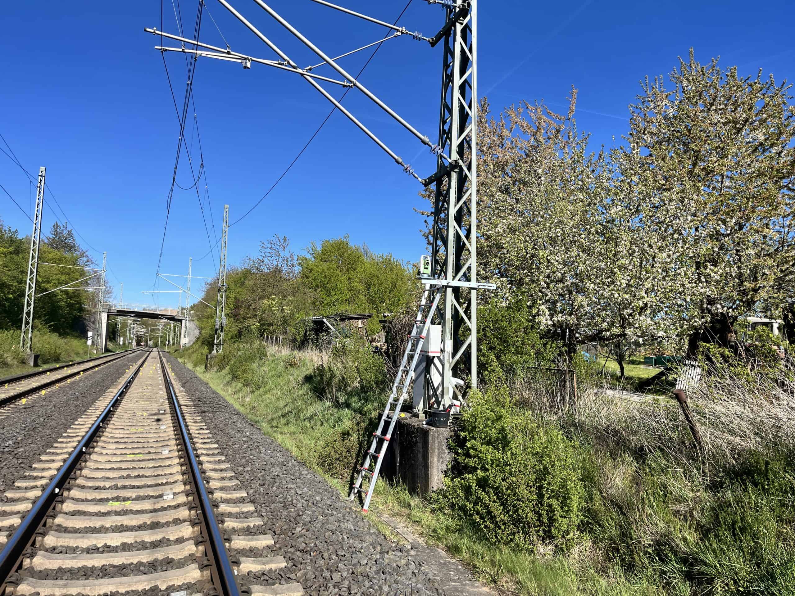 Tachymeter für das Gleismonitoring an einem Oberleitungsmast montiert, mit angelehnter Leiter neben der Bahnstrecke bei Möckmühl